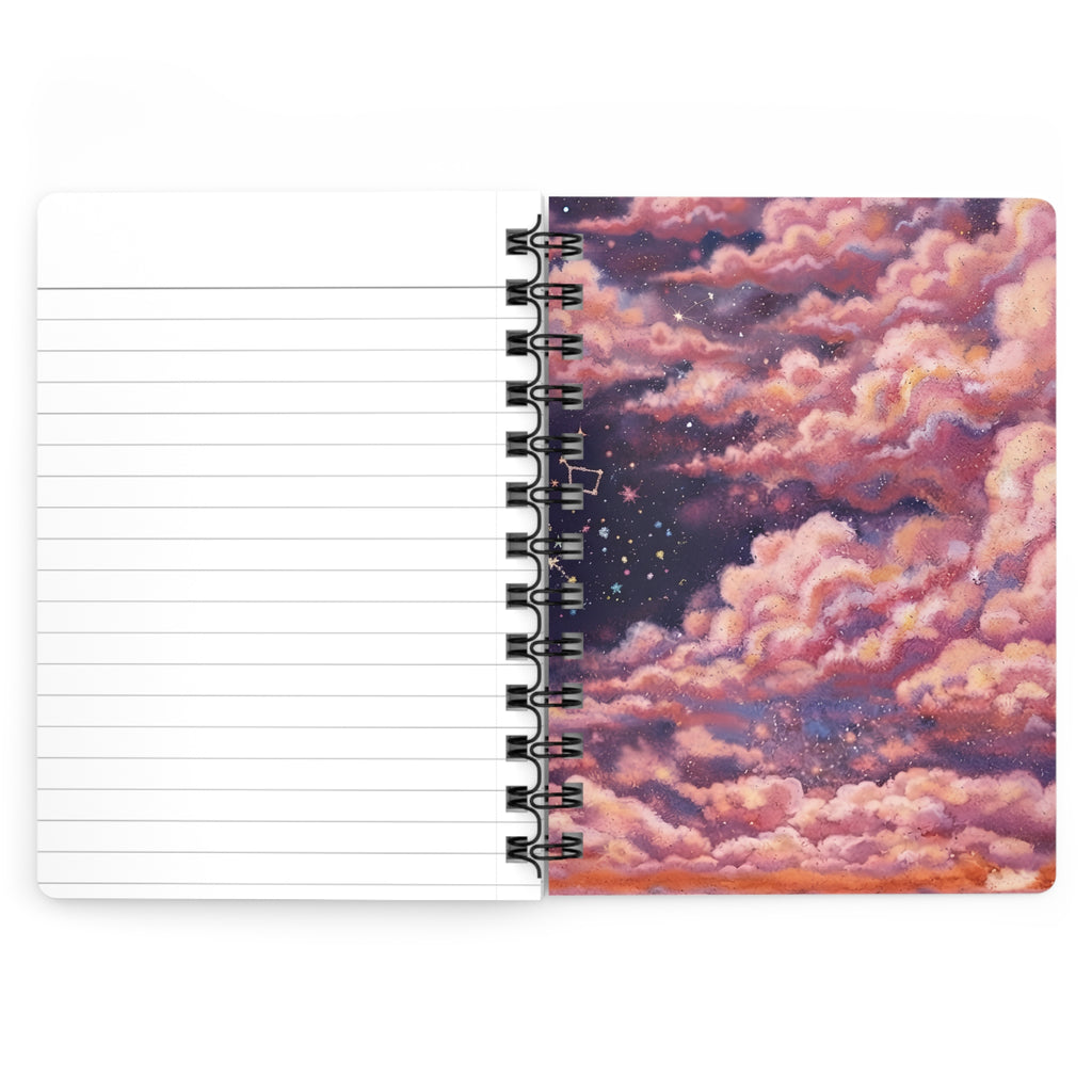 A spiral-bound notebook shown open on a white background, with lined blank pages on the left and a printed cover design on the right featuring pink and purple clouds over a starry night sky.