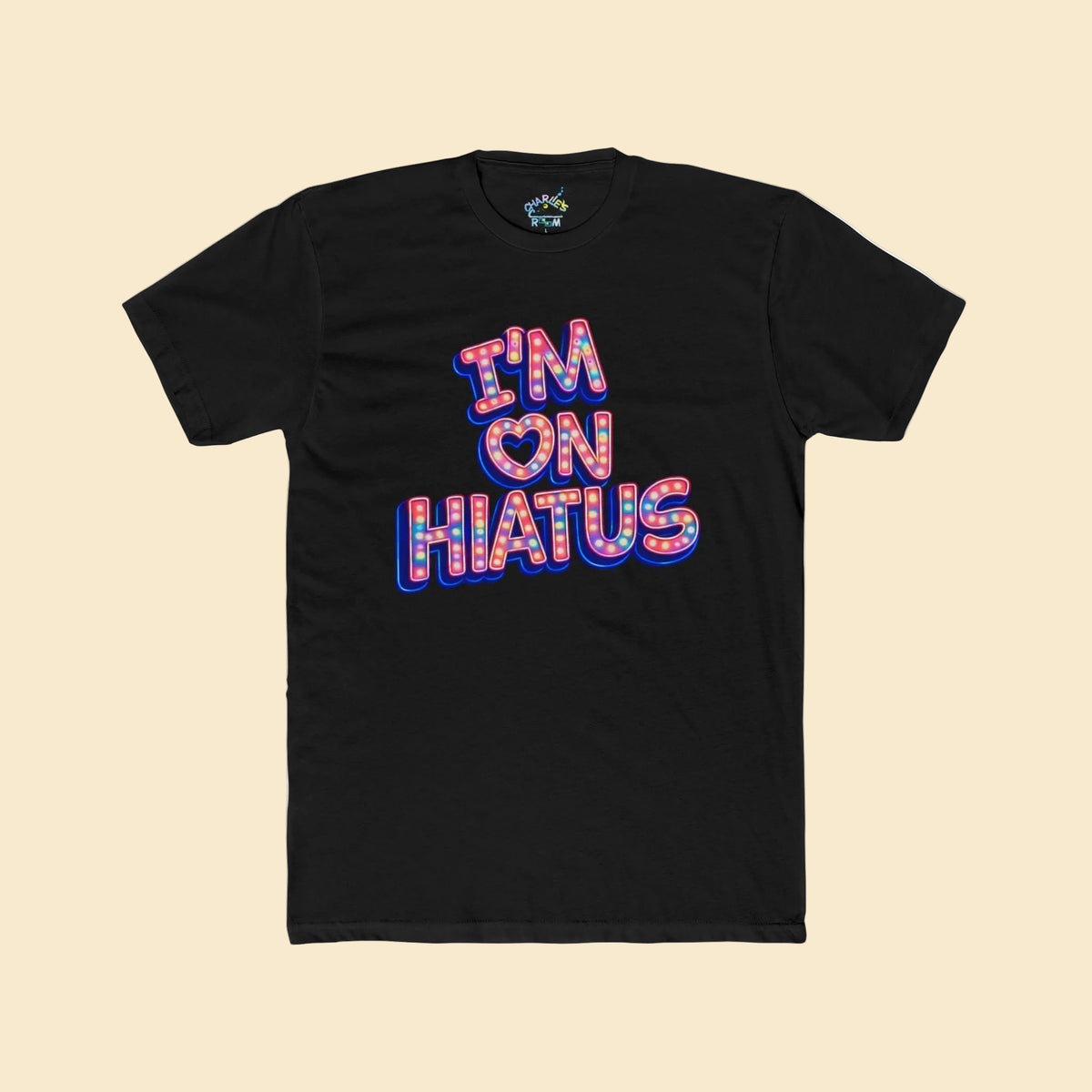 A black short-sleeve t-shirt with a graphic on the chest reading 'I'M ON HIATUS' in a blue, pink, and white marquee-style font with a heart symbol, shown on a soft cream background.