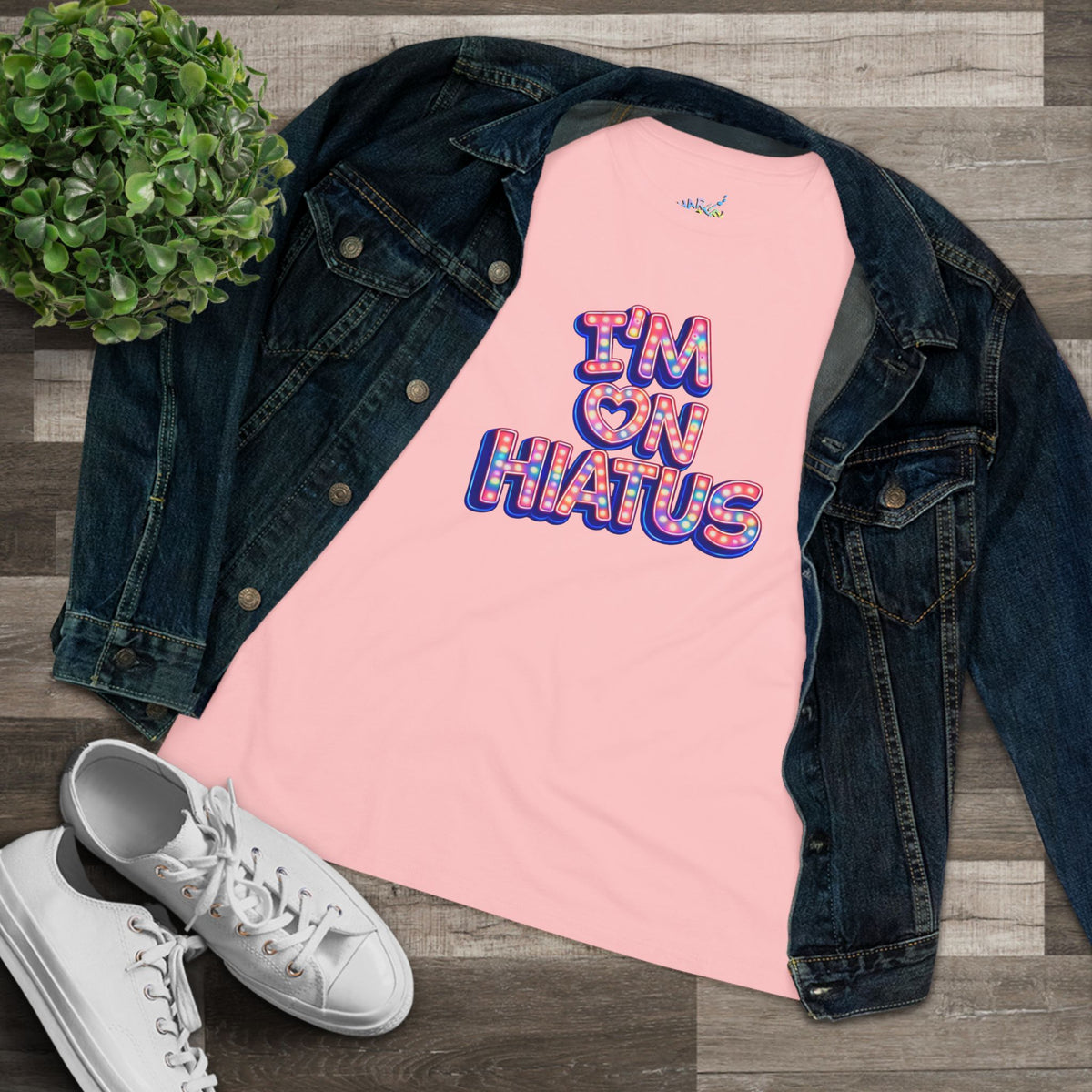 I'm On Hiatus pink graphic t-shirt styled in a flat lay with a denim jacket, white sneakers, and a potted plant.