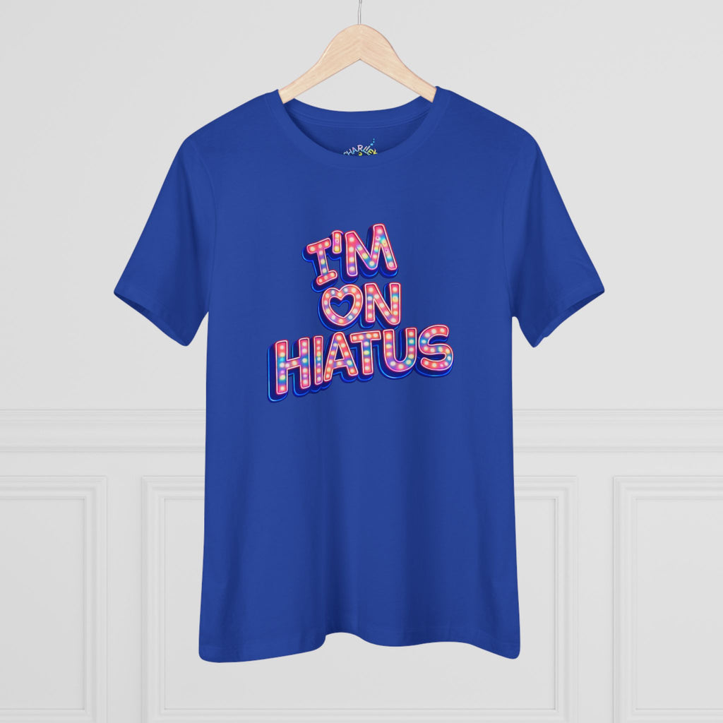 A royal blue short-sleeve t-shirt hanging on a light wood hanger against a white paneled wall. The shirt features the "I'M ON HIATUS" marquee graphic on the chest.